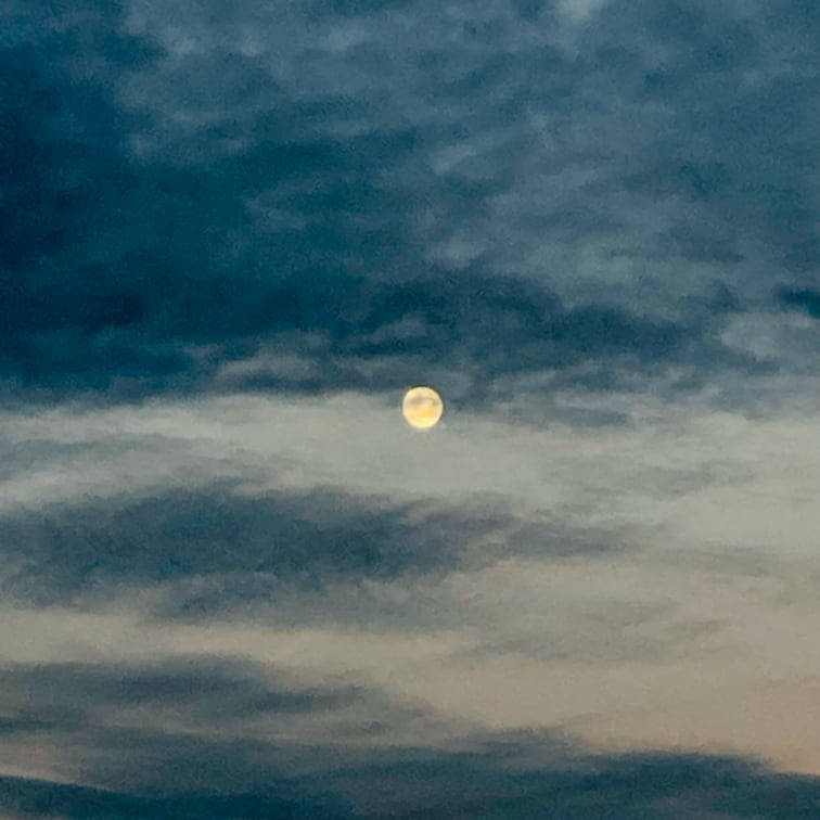 Photo de pleine lune au centre de l’image sur fond de nuages gris-bleu.