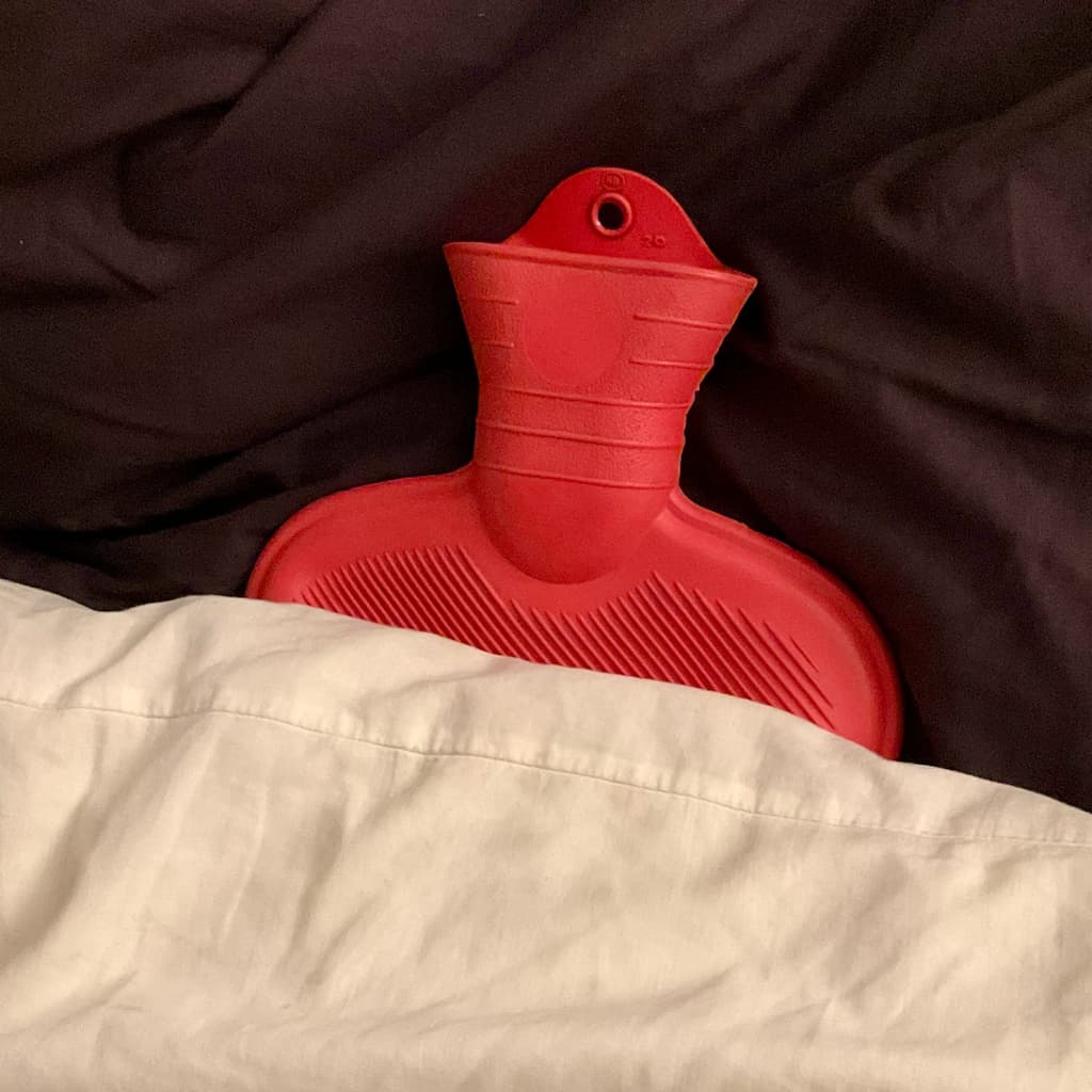 Une bouillote rouge qui dépasse d’une couette blanche contre un oreiller noir.