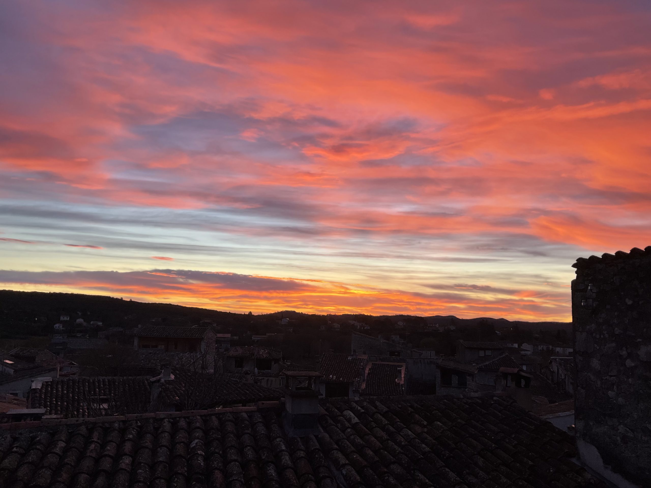ciel rougeoyant à l’aube au dessus des toits encore dans la pénombre de mon village médiéval, pris par la fenêtre de ma chambre